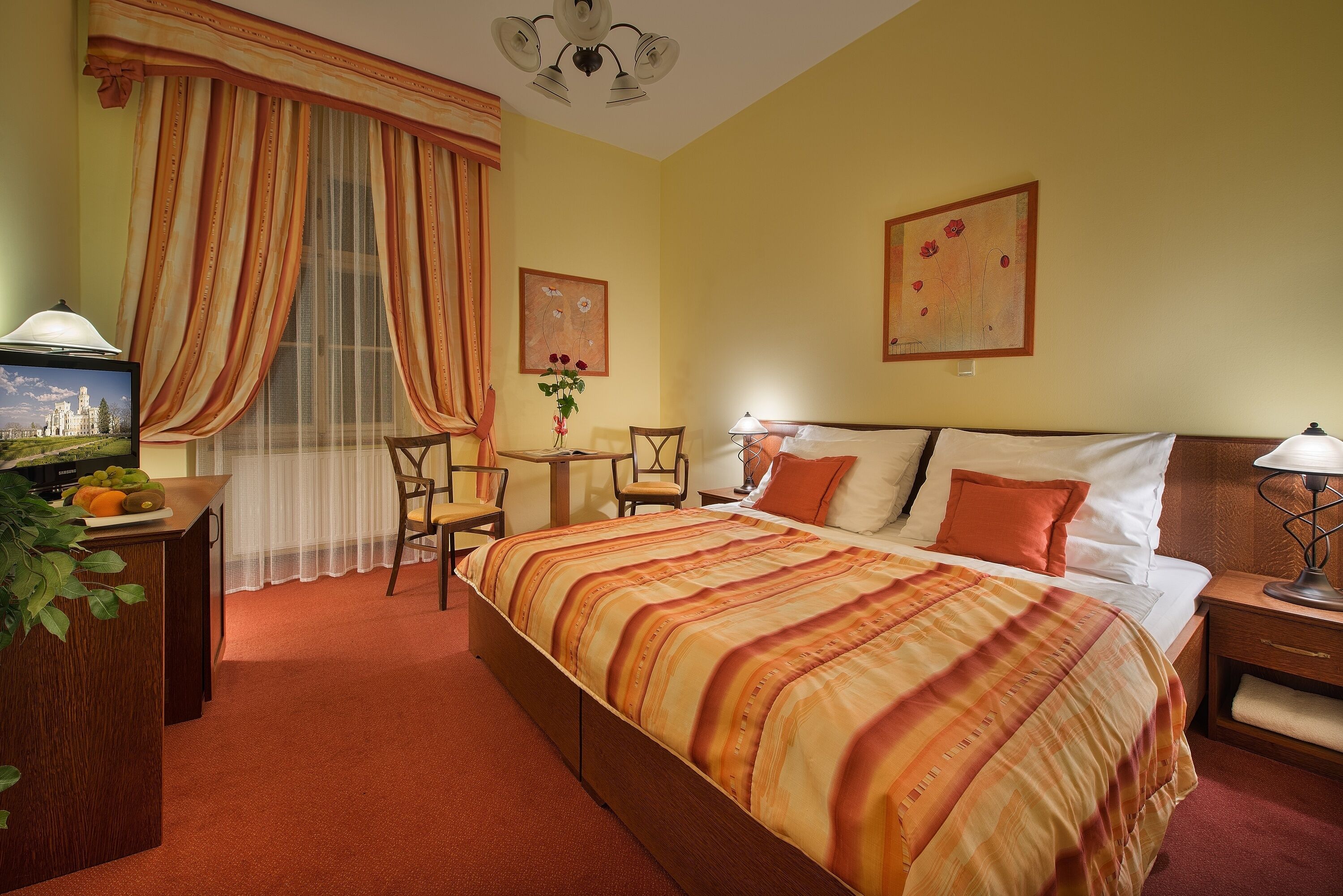 Habitación de hotel con cama, escritorio con lámpara, silla, mesita y un cuadro en la pared.