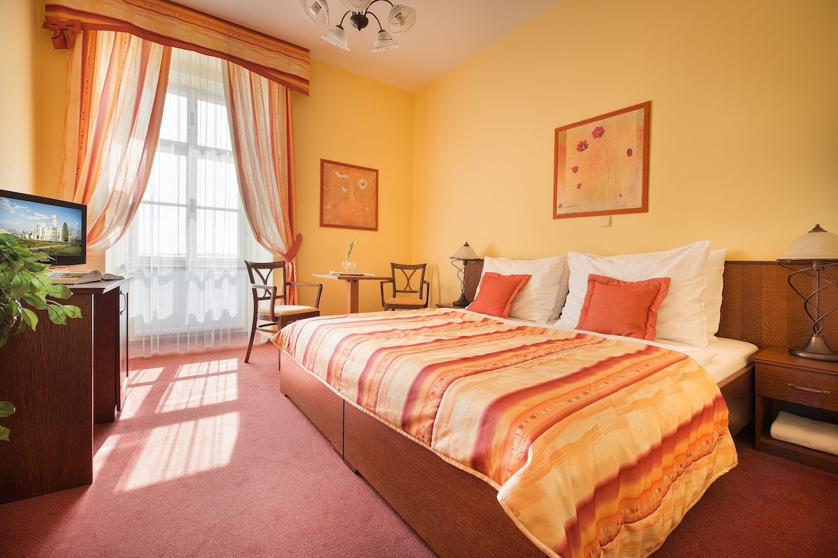 A hotel room with a large bed, a desk, a chair, and a small table.