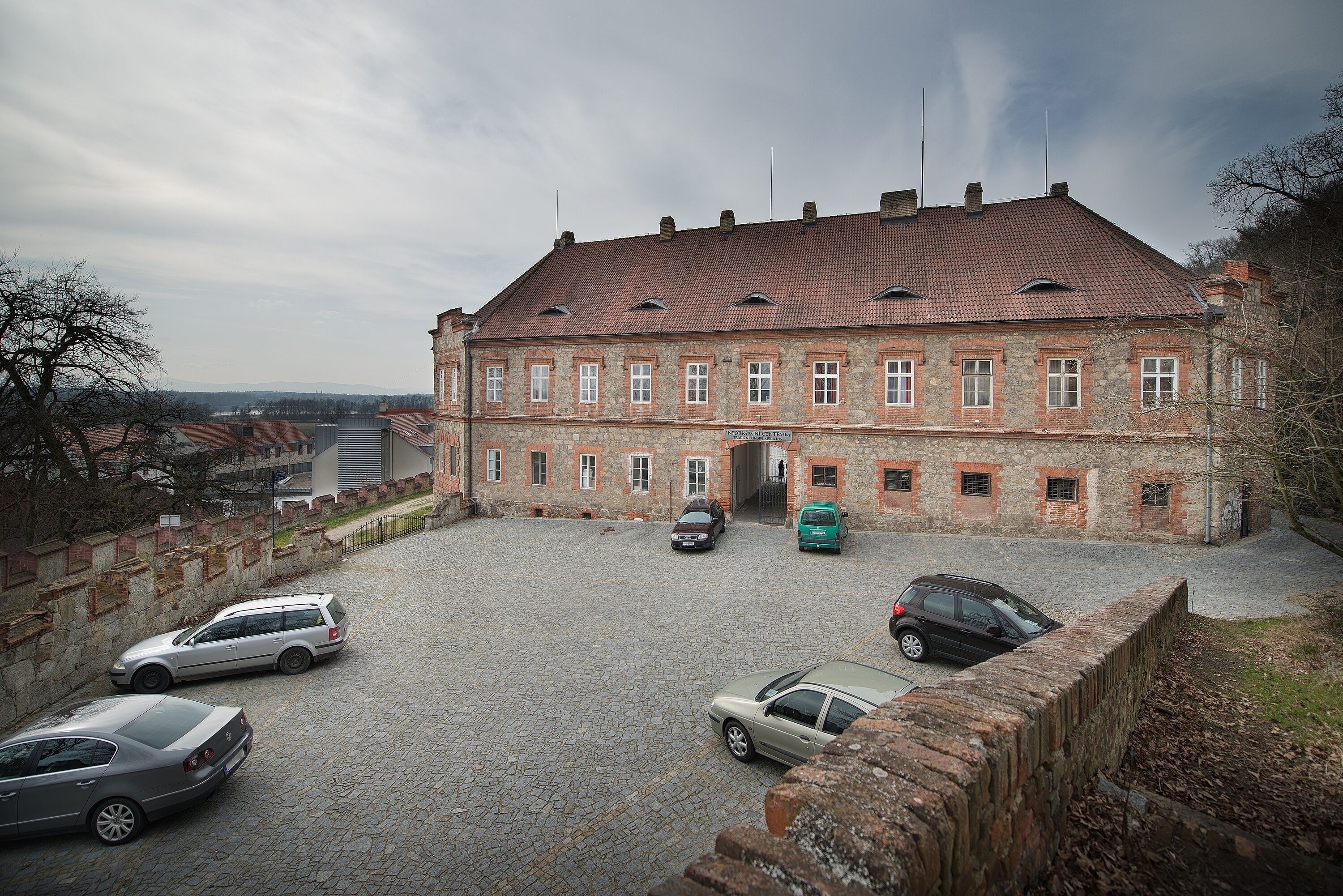 A historic building with a courtyard, stone walls, and parked cars.