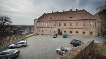 A historic building with a courtyard, stone walls, and parked cars.