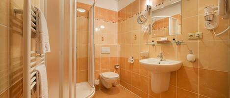 A bathroom with a glass shower enclosure, a toilet, a sink, and a mirror.