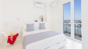 Ein modernes Schlafzimmer mit einem großen Bett, weißen Wänden und einem Balkon mit Blick auf eine Marina.