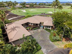 Ein Golfplatz mit Clubhaus, Palmen und freiem Blick auf den Ozean.