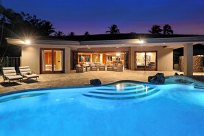 Ein moderner Poolbereich im Freien mit Liegestühlen, einer gut beleuchteten Terrasse und einer Steinmauer.