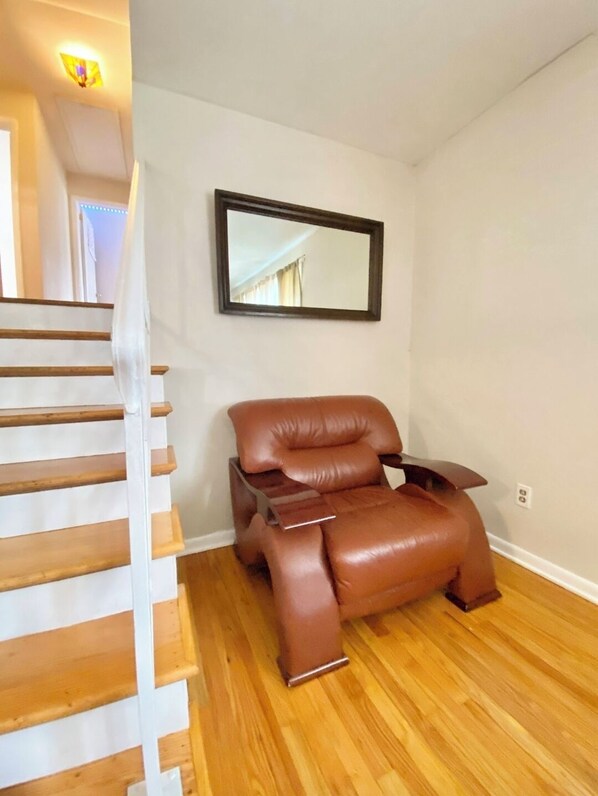 Une pièce avec un escalier en bois, un fauteuil en cuir marron et un miroir fixé au mur.