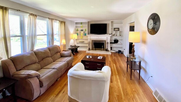 A living room with a sofa, a white armchair, a fireplace, a television, and a clock on the wall. - Spacious 5-bedroom house in welcoming Wilmington with WiFi, AC, Large Yard (Wilmington)