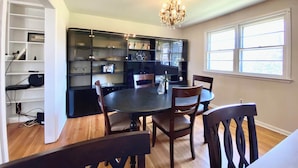 A dining area with a round table, four chairs, a chandelier, and a large window. - Spacious 5-bedroom house in welcoming Wilmington with WiFi, AC, Large Yard (Wilmington)