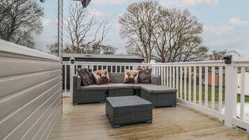 A covered outdoor seating area with a cushioned bench and a sofa, featuring decorative pillows.