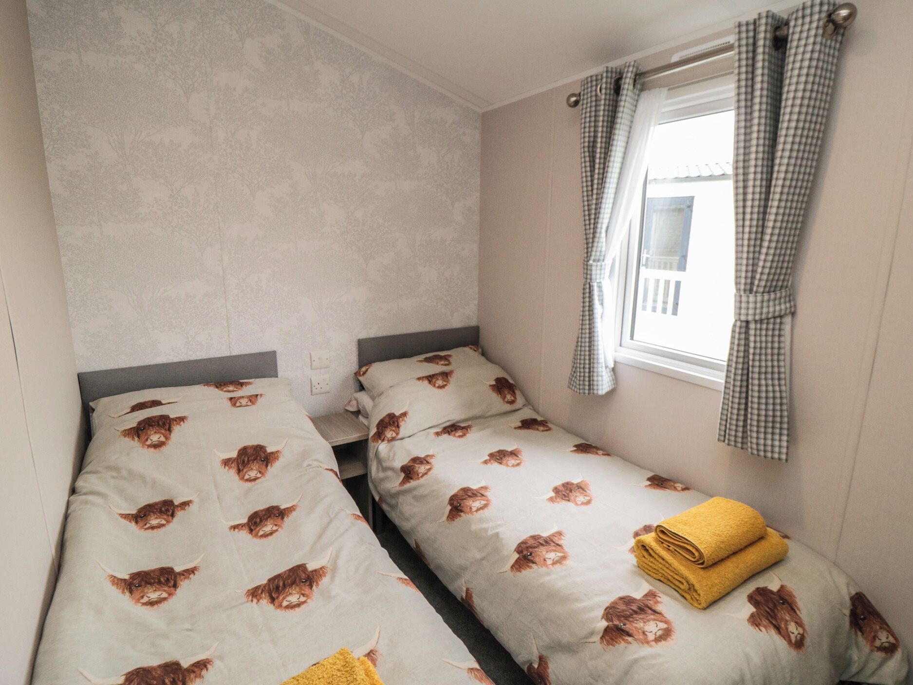 A small, single-room accommodation with two single beds, a window with checkered curtains, and a visible view of the outside.