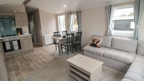 A compact living space with a kitchenette, dining area, and a sofa with a decorative pillow. - Meadow View (Morpeth)