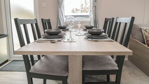 A dining table with four chairs, two wine glasses, and plates set for four. - Meadow View (Morpeth)
