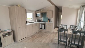 A compact kitchen with light wood cabinets, a built-in microwave, and a dining area with a table and chairs. - Meadow View (Morpeth)