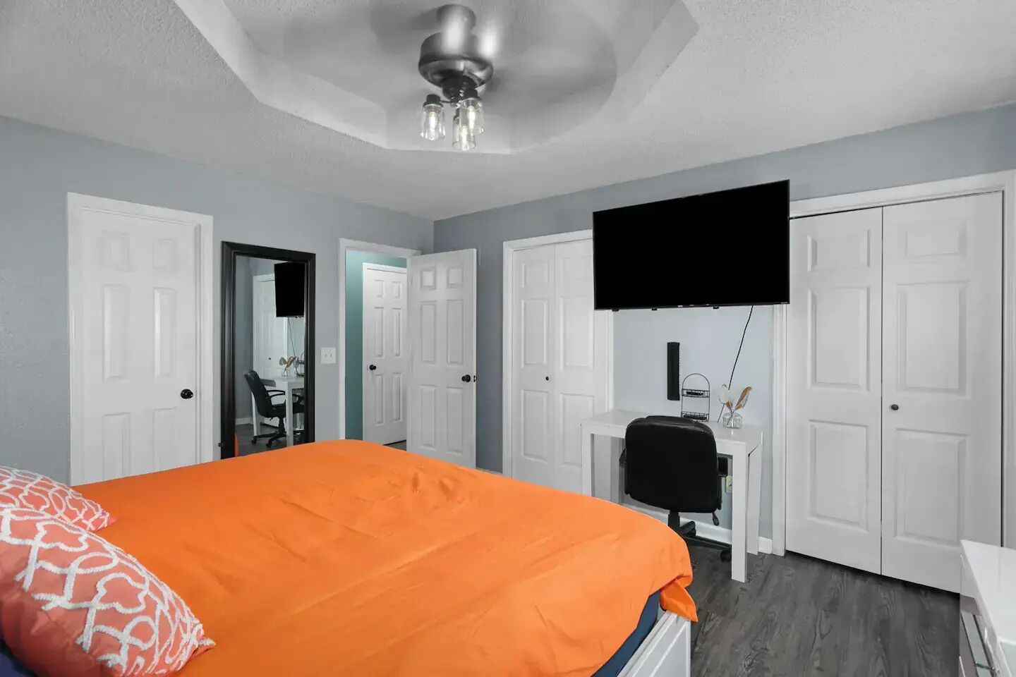 Een slaapkamer met een bed, een bureau, een stoel en een aan de muur bevestigde televisie.