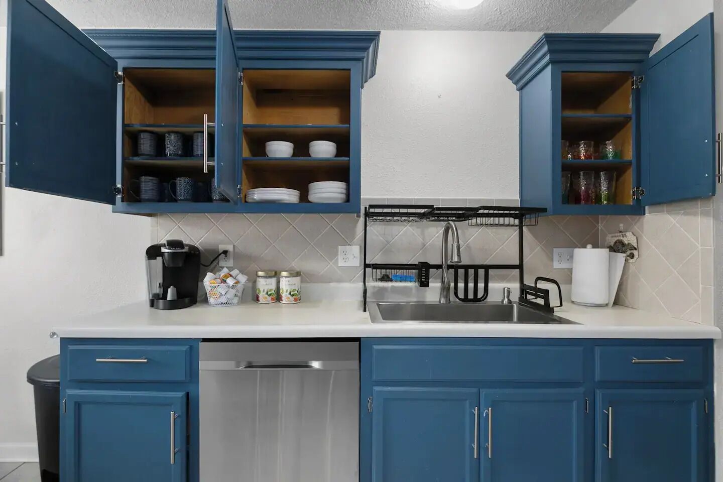 A kitchen with blue cabinets, a stainless steel sink, and a coffee maker.