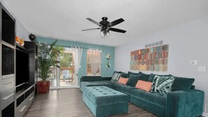 A living room with a teal sofa, a ceiling fan, and a TV.