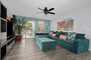 Un salon avec un canapé de couleur turquoise, un ventilateur de plafond et un téléviseur.