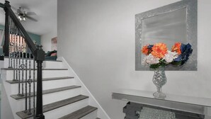 A staircase with a black railing and wooden steps, leading to a landing with a decorative mirror and a vase of flowers.