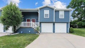 A two-story residential building with a covered front porch, two garage doors, and a well-maintained lawn.