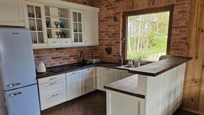 A kitchen with white cabinetry, a built-in island, a refrigerator, and a window with a view of trees.