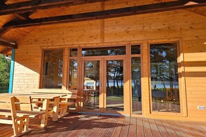 Eine Holzhütte mit einer Terrasse, großen Glasfenstern und Sitzgelegenheiten im Freien.
