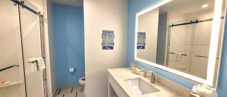 A modern bathroom with a large mirror, a shower area, and a vanity with a sink and towel rack.