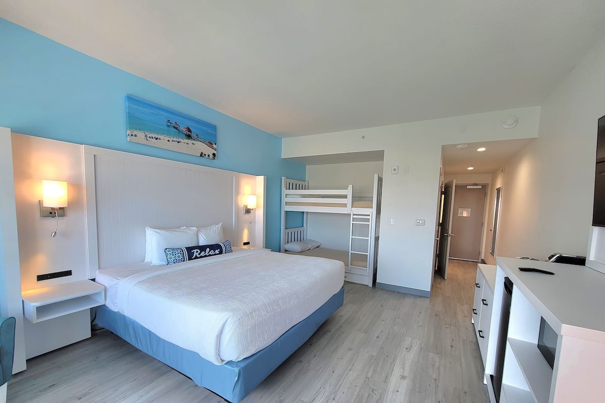 Une chambre avec un lit superposé, un bureau, une chaise, une table de chevet et une lampe fixée au mur.