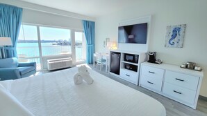 Hotellihuone, jossa on suuri sänky, televisio, minibaari ja näkymä merelle.