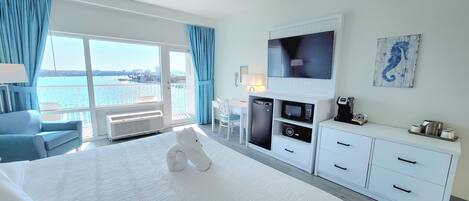 A hotel room with a large bed, a TV, a minibar, and a view of the sea.
