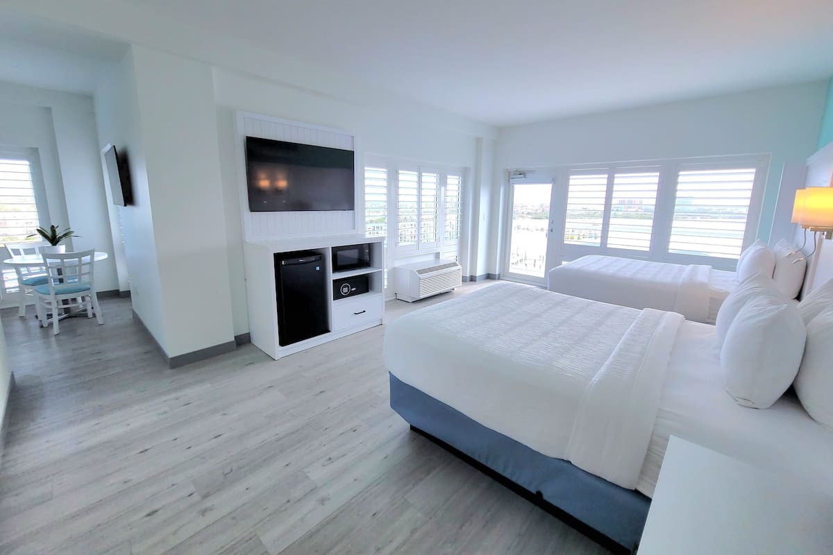 Une chambre d’hôtel moderne dotée d’un grand lit, d’un téléviseur à écran plat fixé au mur, d’un petit coin salon avec une table et des chaises, et d’un balcon avec vue.