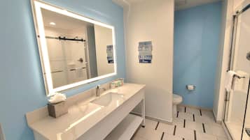 A modern bathroom with a large mirror, two sinks, a shower, and a toilet.