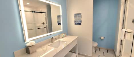 A modern bathroom with a large mirror, two sinks, a shower, and a toilet.