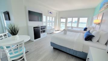 Habitación de hotel moderna con una cama grande, un televisor, un escritorio con computadora y vistas a la ciudad a través de las ventanas.