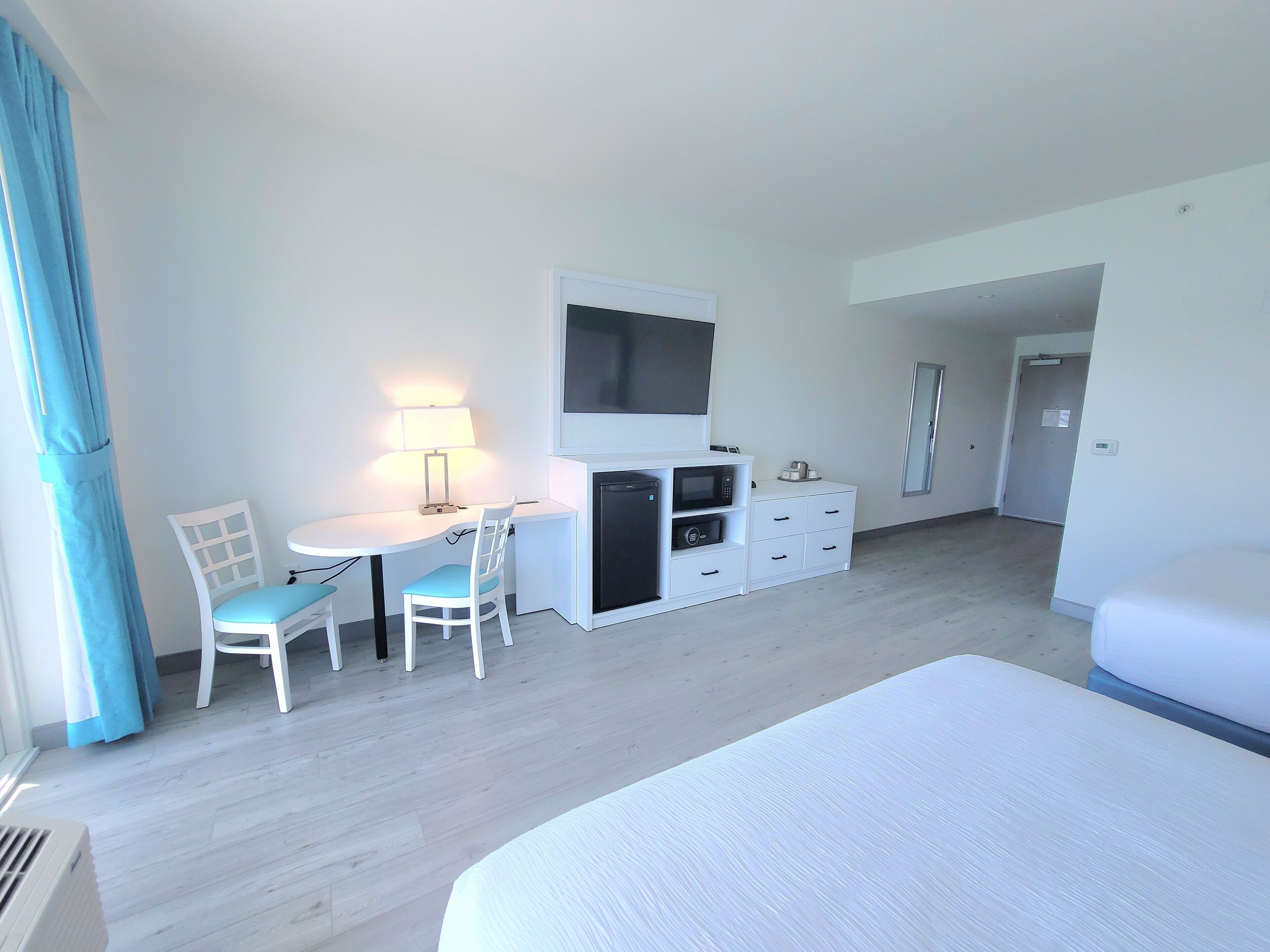 Habitación de hotel con cama, escritorio y silla, televisor, refrigerador pequeño y cómoda.