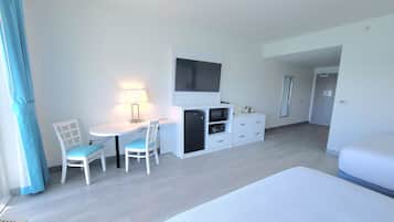 A hotel room with a bed, a desk with a chair, a TV, a mini-fridge, and a dresser.