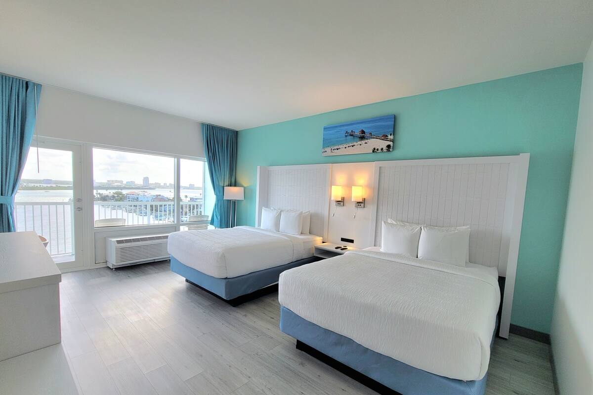 Une chambre d’hôtel avec deux lits, une vue sur la ville et un balcon donnant sur l’eau.