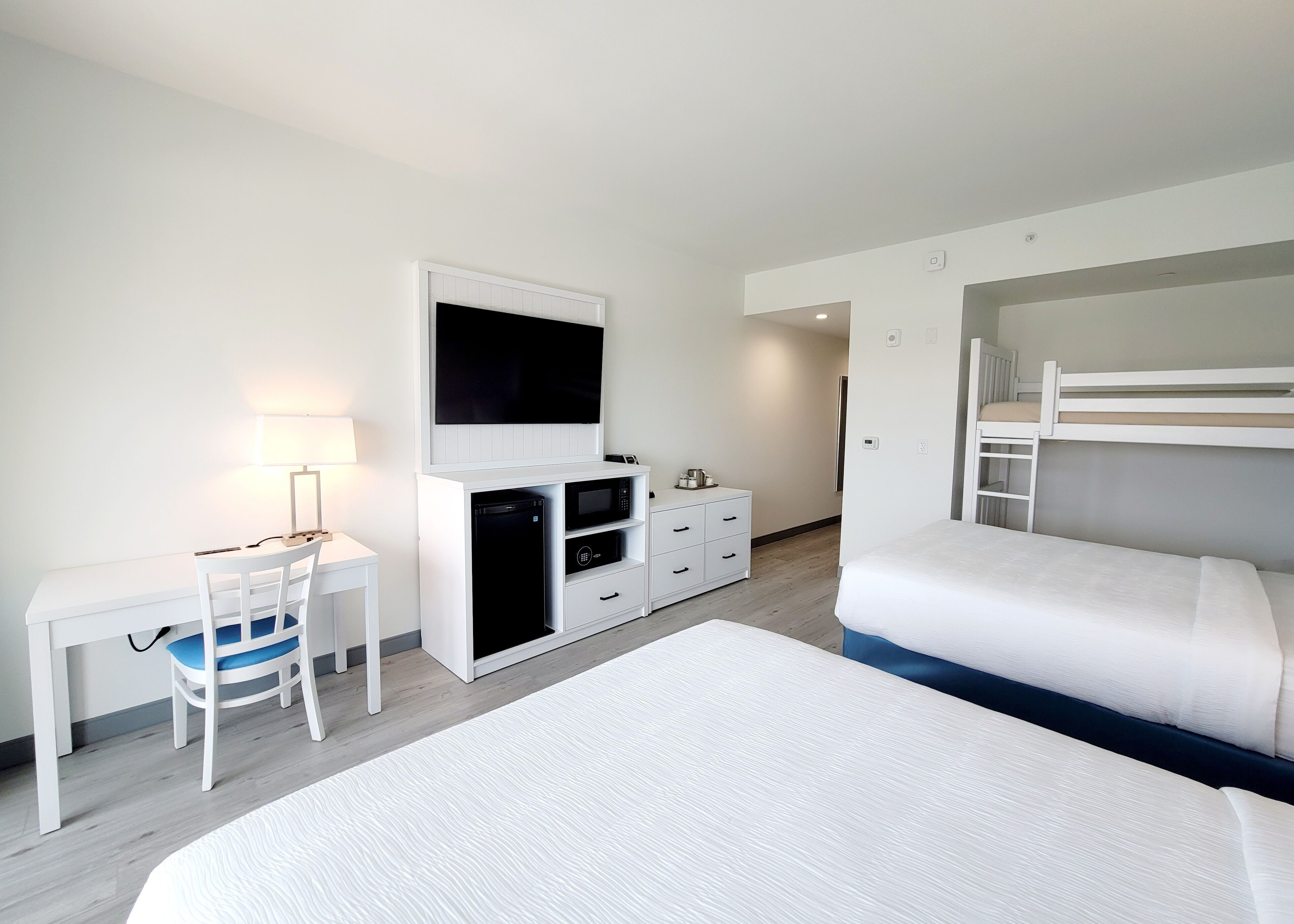 A hotel room with a bed, a desk with a chair, a TV, a microwave, and a small refrigerator.