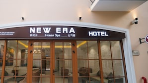 Een hotelingang met een glazen deur, een bord boven de deur en een buitenkraan rechts.