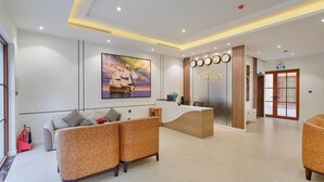 Een moderne receptie met een receptiebalie, een groot schilderij, een zithoek met banken, en een decoratieve wand met klokken.
