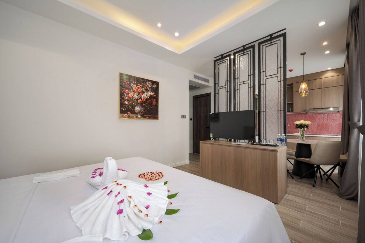 Ein Hotelzimmer mit einem ordentlich bezogenen Bett, einem Schreibtisch mit einem Flachbildfernseher, einem kleinen Tisch mit einer Vase und einem Bild an der Wand.