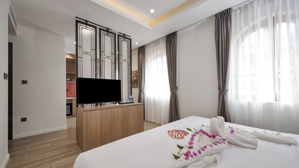 Een hotelkamer met een net opgemaakt bed, een flatscreen televisie op een houten bureau, en uitzicht op de gang en een andere kamer.
