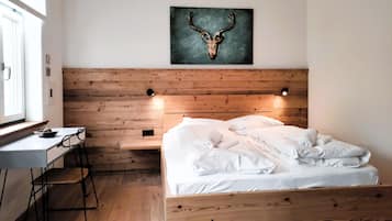 Ein Schlafzimmer mit hölzernem Kopfteil, einem Bett mit weißen Leinentüchern, einem Schreibtisch mit Stuhl und einem Wandbild mit einem Hirschschädel.