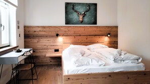 A bedroom with a wooden headboard, a bed with white linens, a desk with a chair, and a wall-mounted artwork of a deer skull. - "Bergstift", Oberstaufen/Höfen (Oberstaufen)