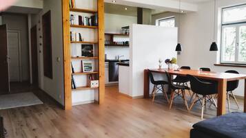 Eine moderne Küche mit Holzschränken, ein Essbereich mit Holztisch und -stühlen sowie ein Bücherregal mit Büchern und Dekoration.