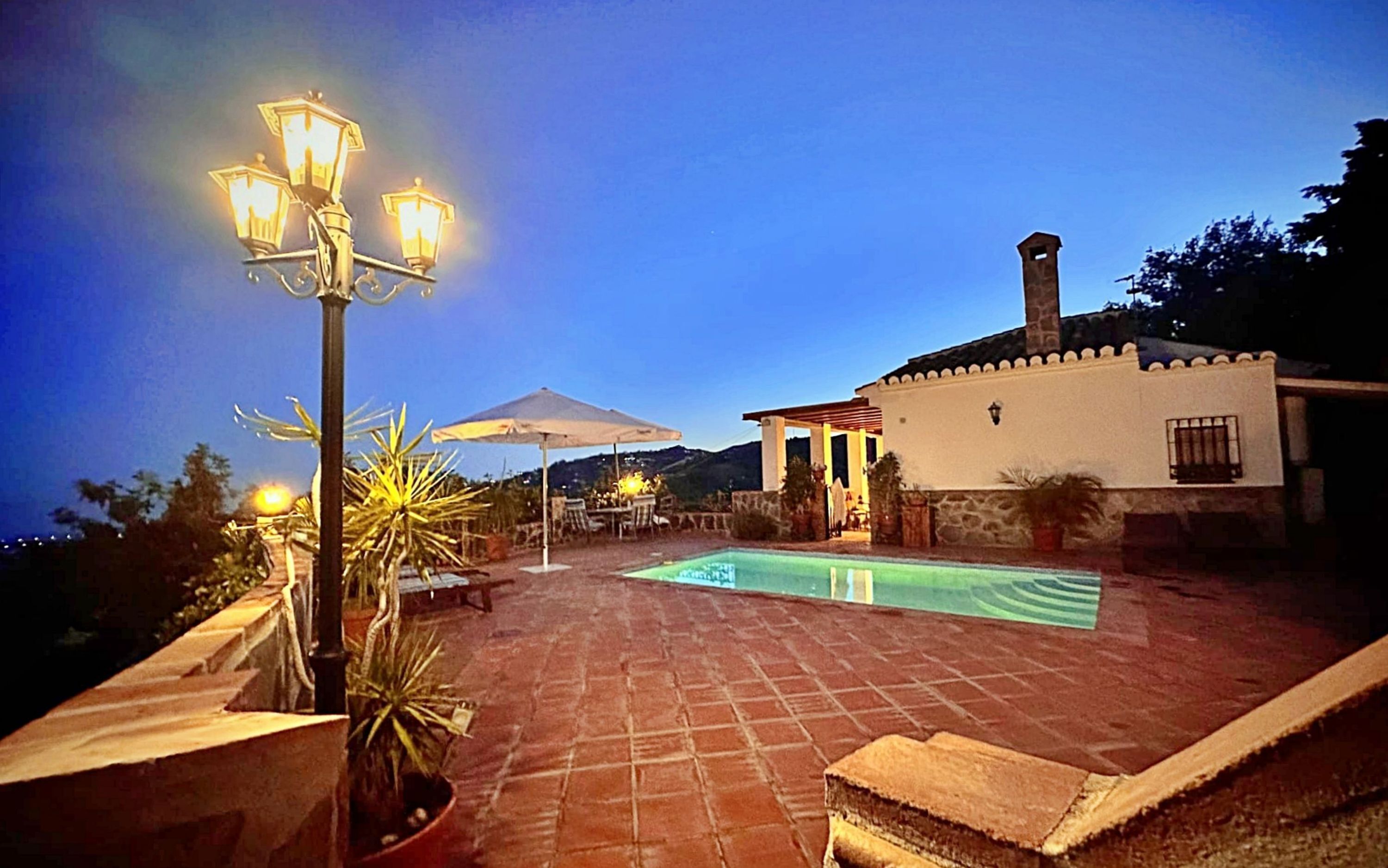 A rooftop pool area with a pergola, lounge chairs, and a street lamp.
