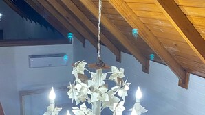 A chandelier with multiple lights hanging from a wooden ceiling in a room with white walls and a visible air conditioning unit.