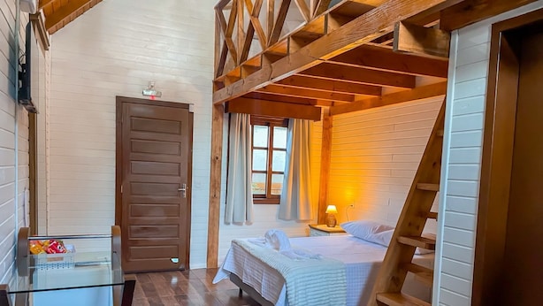 A cozy room with a bed, a nightstand, a lamp, a wooden ladder, and a glass table with snacks.