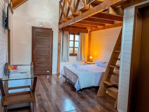 A cozy room with a bed, a nightstand, a lamp, a wooden ladder, and a glass table with snacks. - Chalés dos Pássaros (Gramado)
