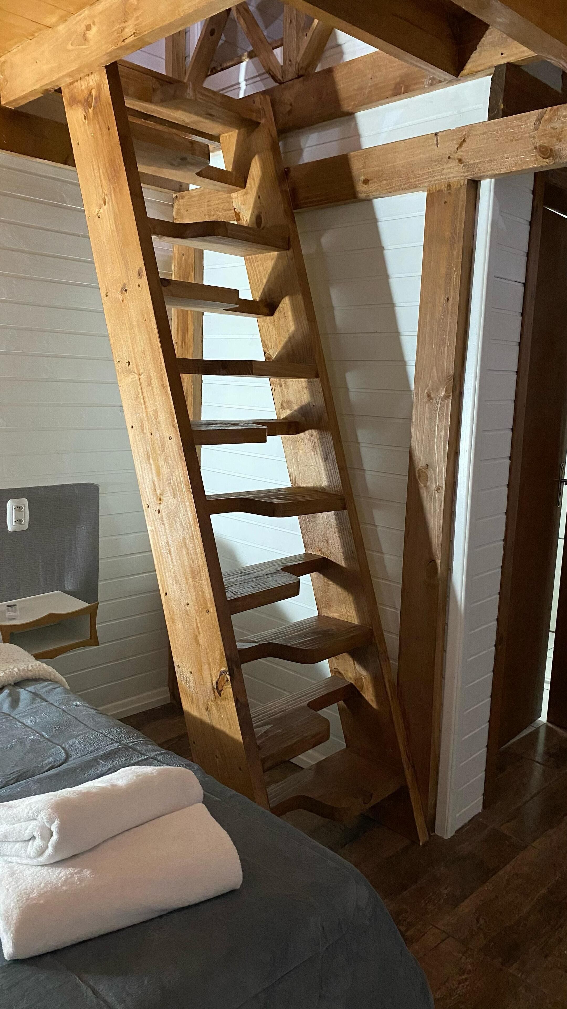 Dormitorio estilo loft con escalera de madera, cama y mesita de noche.