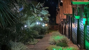 A pathway flanked by lush greenery and a building with a tiled roof.