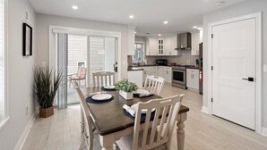 Een moderne keuken met witte kasten, een eethoek met een houten tafel en stoelen, en een witte deur.